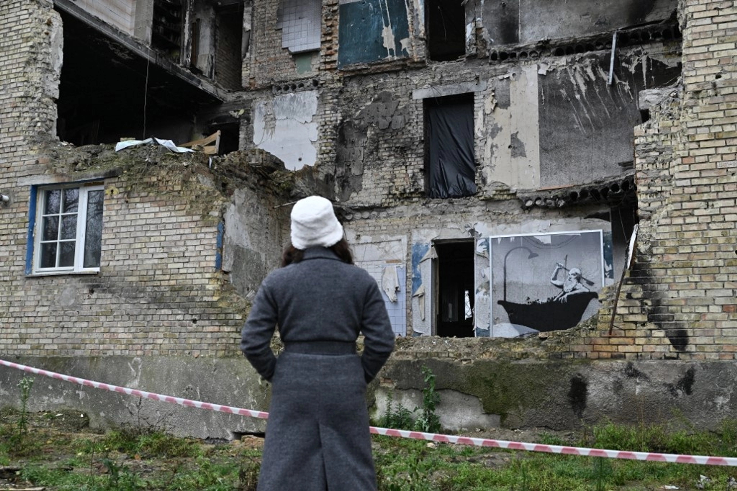 A woman looks at a graffiti made by Banksy on the wall of a heavily damaged building in the Gorenka village.