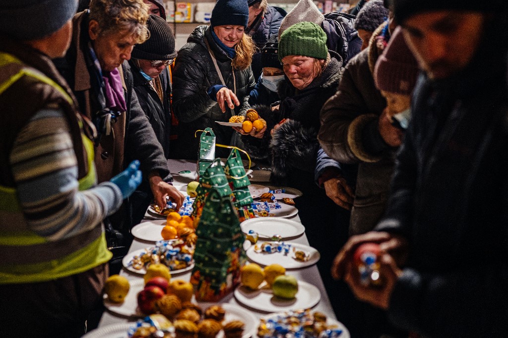 Local residents gather around an impromptu Christmas Eve table to serve themselves to small cakes and fruit, at a humanitarian aid centre in Bakhmut, Donetsk region, on January 6, 2023. AFP