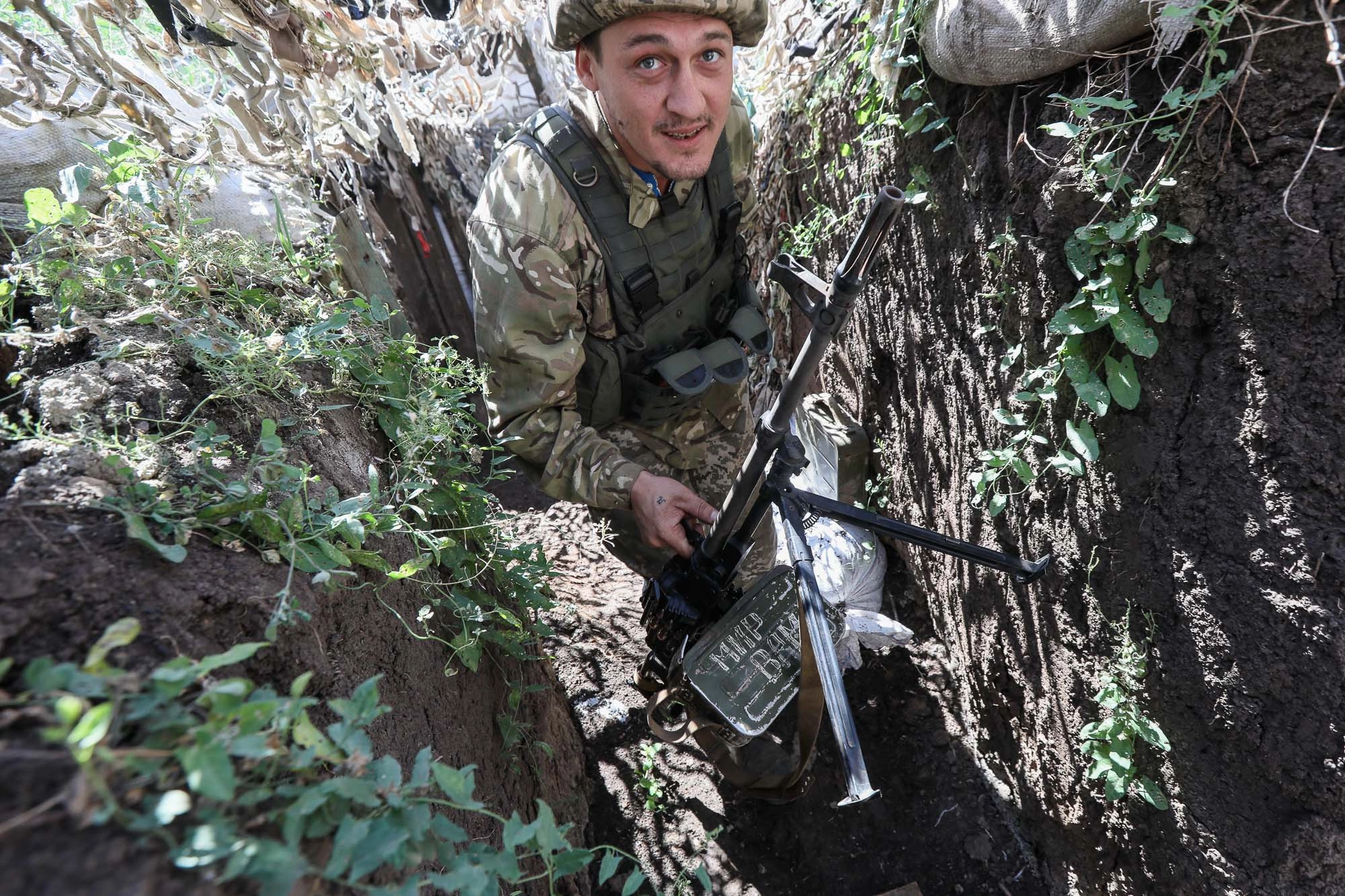 A Ukrainian soldier carries a machine gun to a combat post as he walks along a trench line in the town of Zaitseve on June 25