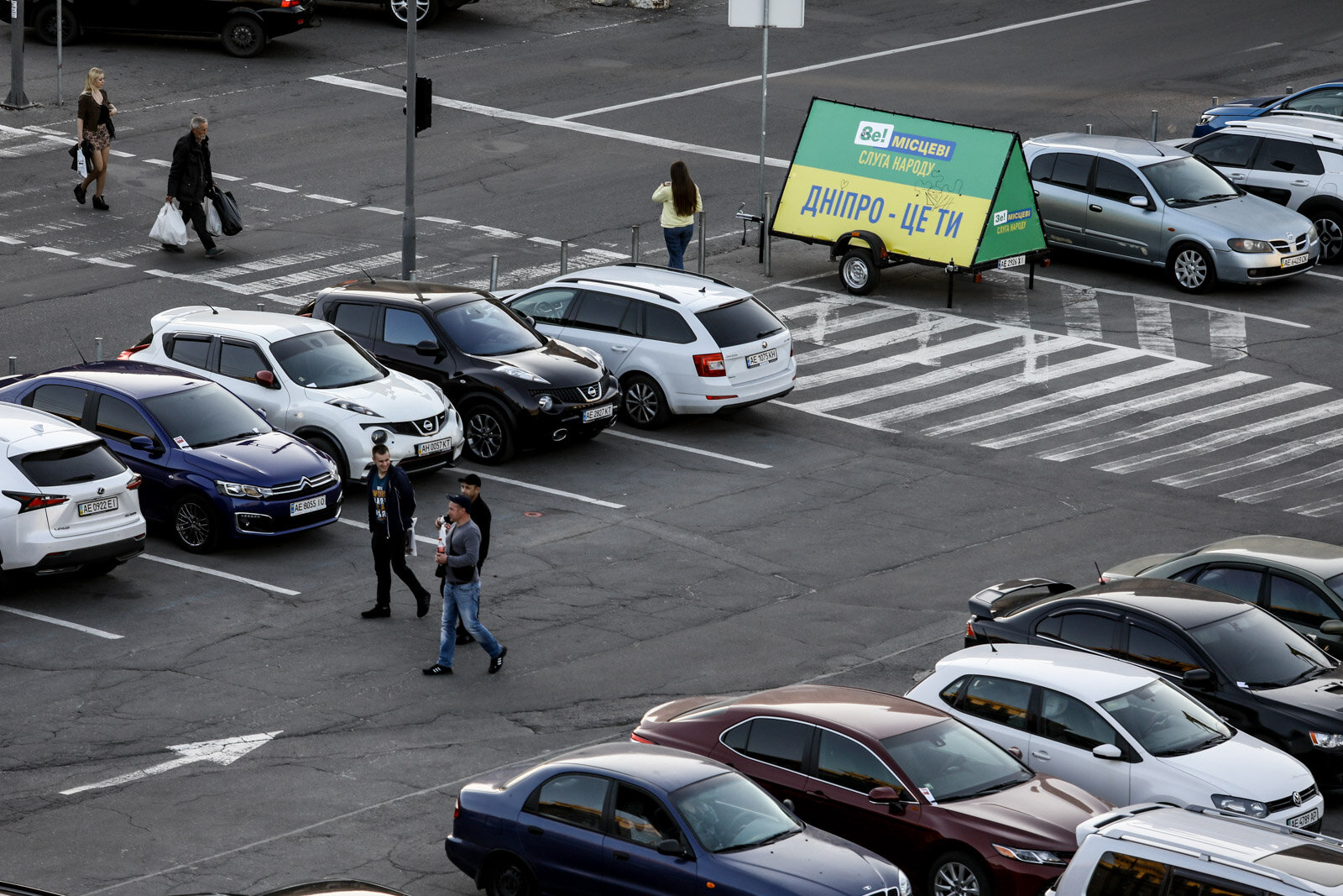 People walk through a parking lot near the Servant of the People party campaign banner in Dnipro, on Oct. 6, 2020. Street ads of the Servant of the People party are unofficially banned in the city.