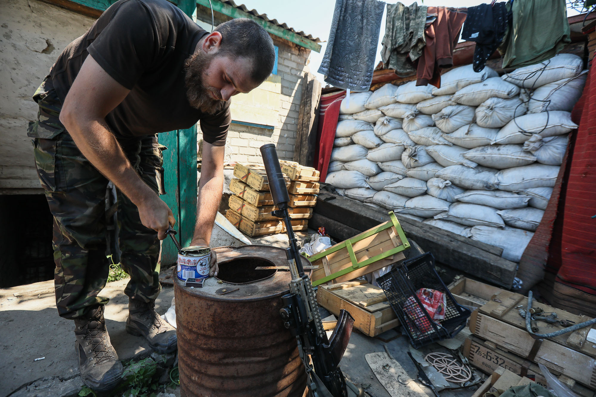 A Ukrainian soldier pries open a canned meat to feed cats at a combat post in the town of Zaitseve on June 25