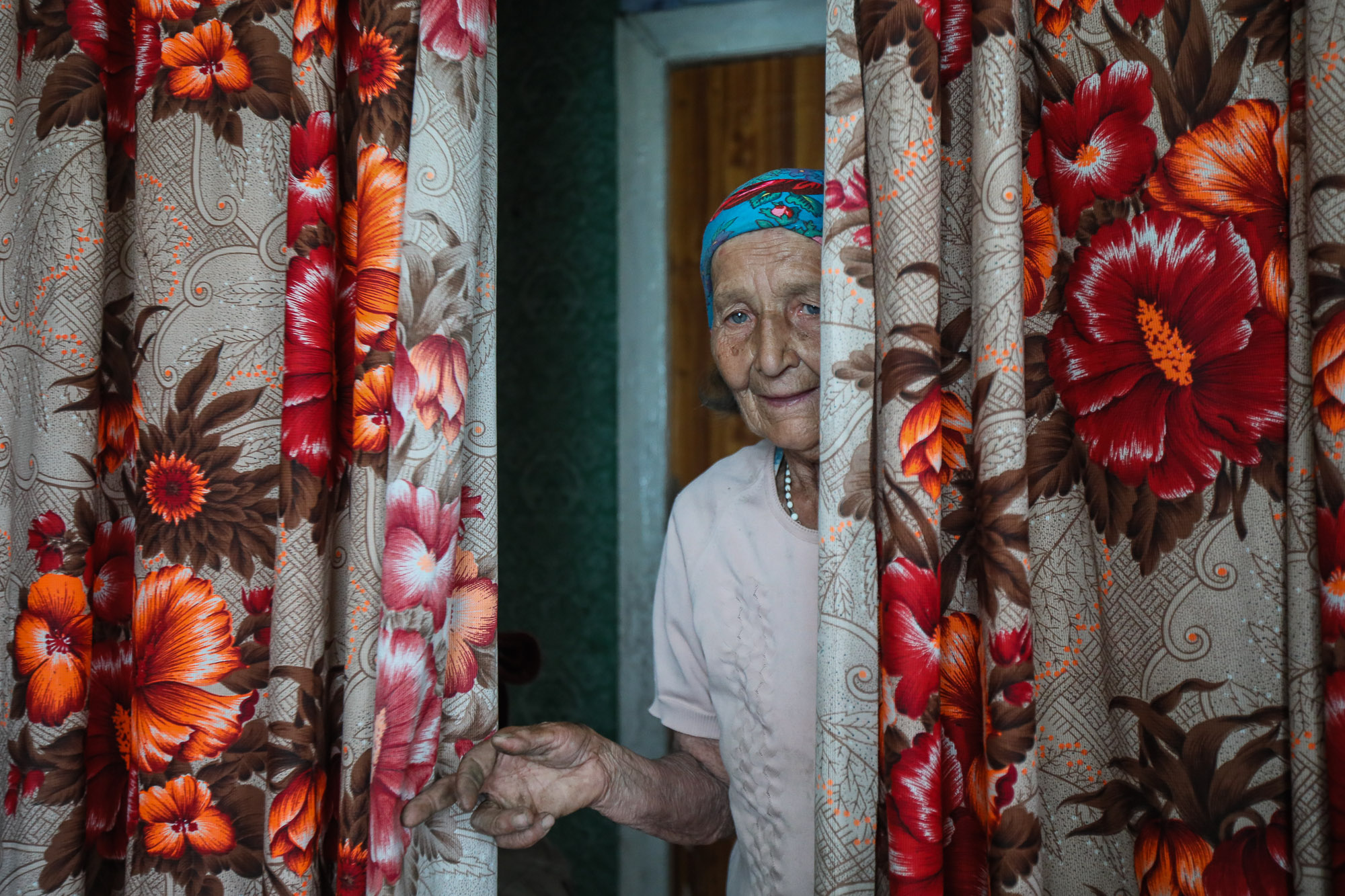 Mariya Horpynych, a elderly local civilian, looks out from behind curtains in her house in the town of Opytne, eastern Ukraine, on June 12, 2019.