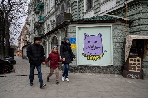A family walks in front of a street art creation by the LBWS street art collective on a street in the port city of Odesa on April 13, 2022. (Photo by Ed JONES / AFP)