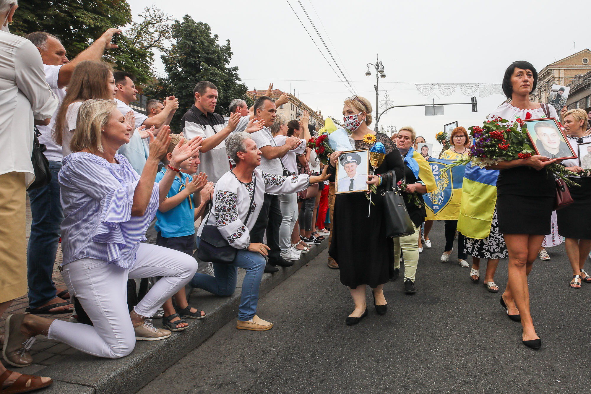 People kneel as Ukrainians carry portraits of fallen soldiers during the March of Defenders of Ukraine, an event that celebrated Ukraine&#8217;s Independence Day in Kyiv on Aug. 24, 2020.