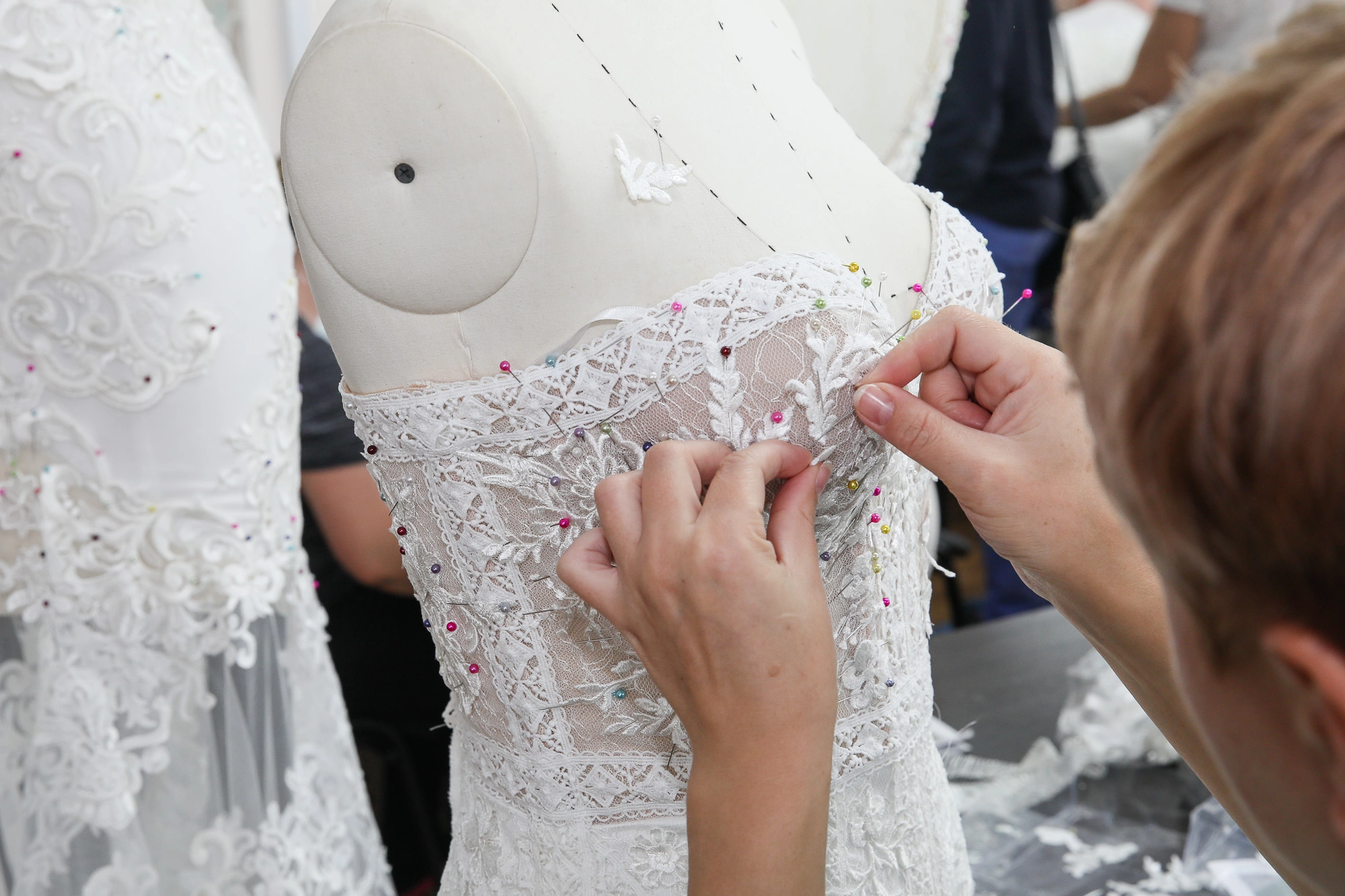 A seamstress pins lace onto a future wedding dress. This is the most expensive part of the dress to create. 