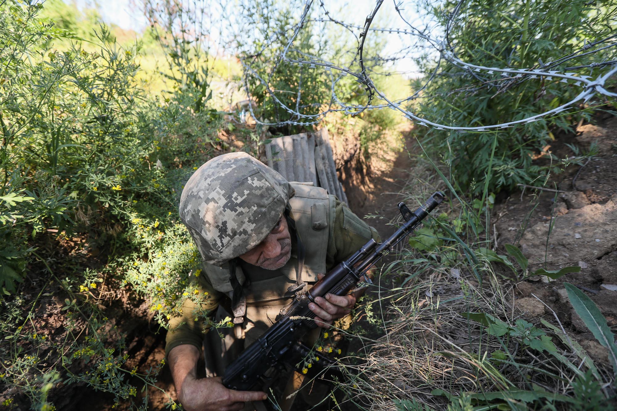 A Ukrainian soldier climbs under a barbed wire line along a trench leading to a combat post in the town of Zaitseve on June 25  