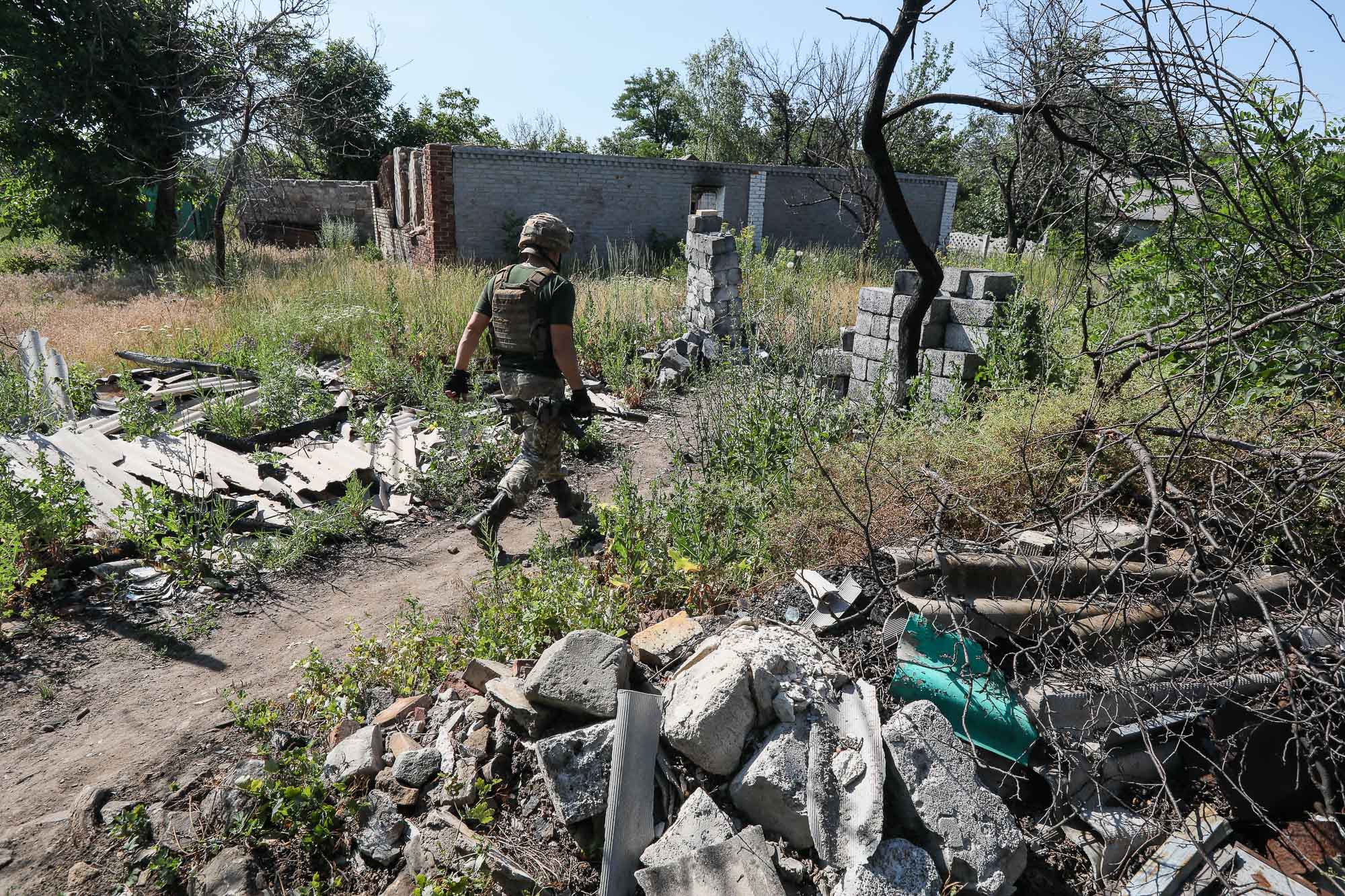 A Ukrainian soldier walks along ruined houses in the town of Zaitseve on June 25, 2018.