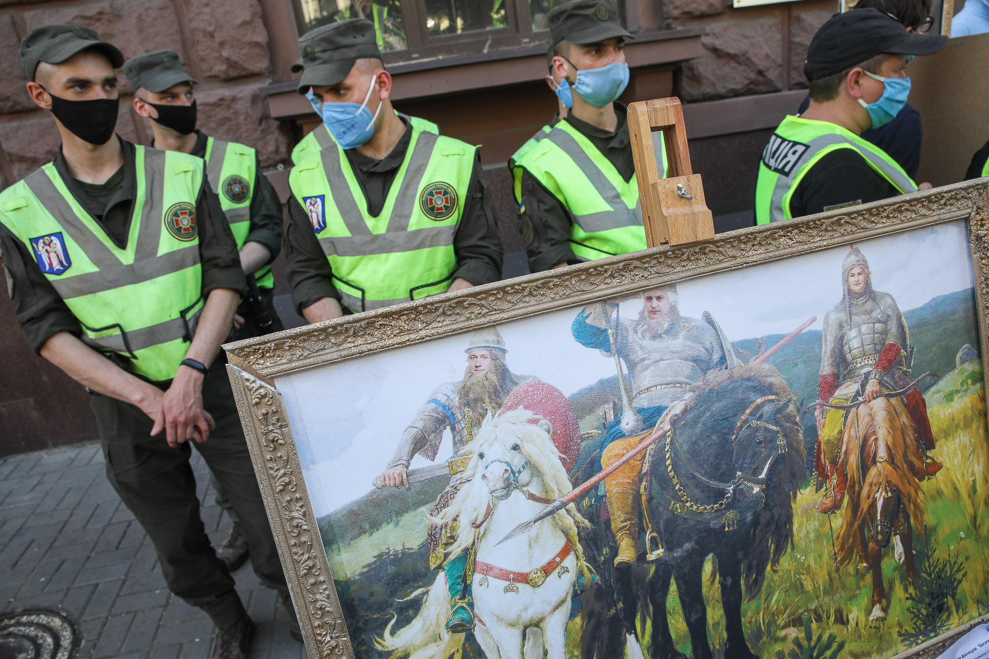 National guards stand with police officers as activists and supporters of European Solidarity political party and Petro Poroshenko hold mockup pictures of classic art masterpieces with the faces of Prosecutor General Iryna Venediktova and President Volodymyr Zelensky during a rally in front of the State Investigation Bureau in downtown Kyiv on June 10, 2020.