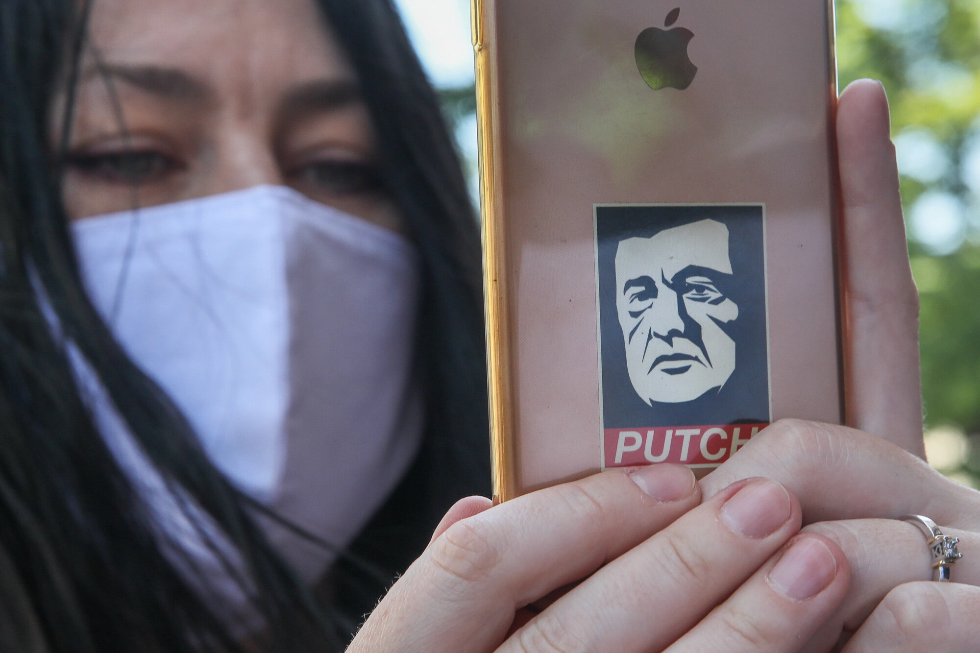 A woman streams online video holding a phone with a picture of Petro Poroshenko as activists and supporters of the European Solidarity political party and Petro Poroshenko hold mockup pictures of classic art masterpieces with the faces of Prosecutor General Iryna Venediktova and President Volodymyr Zelensky during a rally in front of the State Investigation Bureau in downtown Kyiv on June 10, 2020.