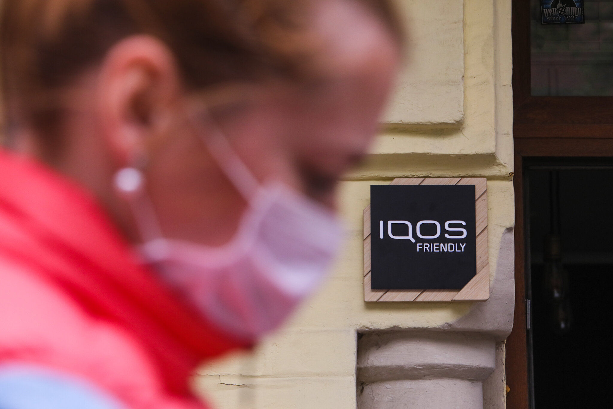 A woman wearing a medical mask walks by an entrance to an “IQOS-friendly” restaurant that allows indoor IQOS puffing on May 15, 2020 in Kyiv.
