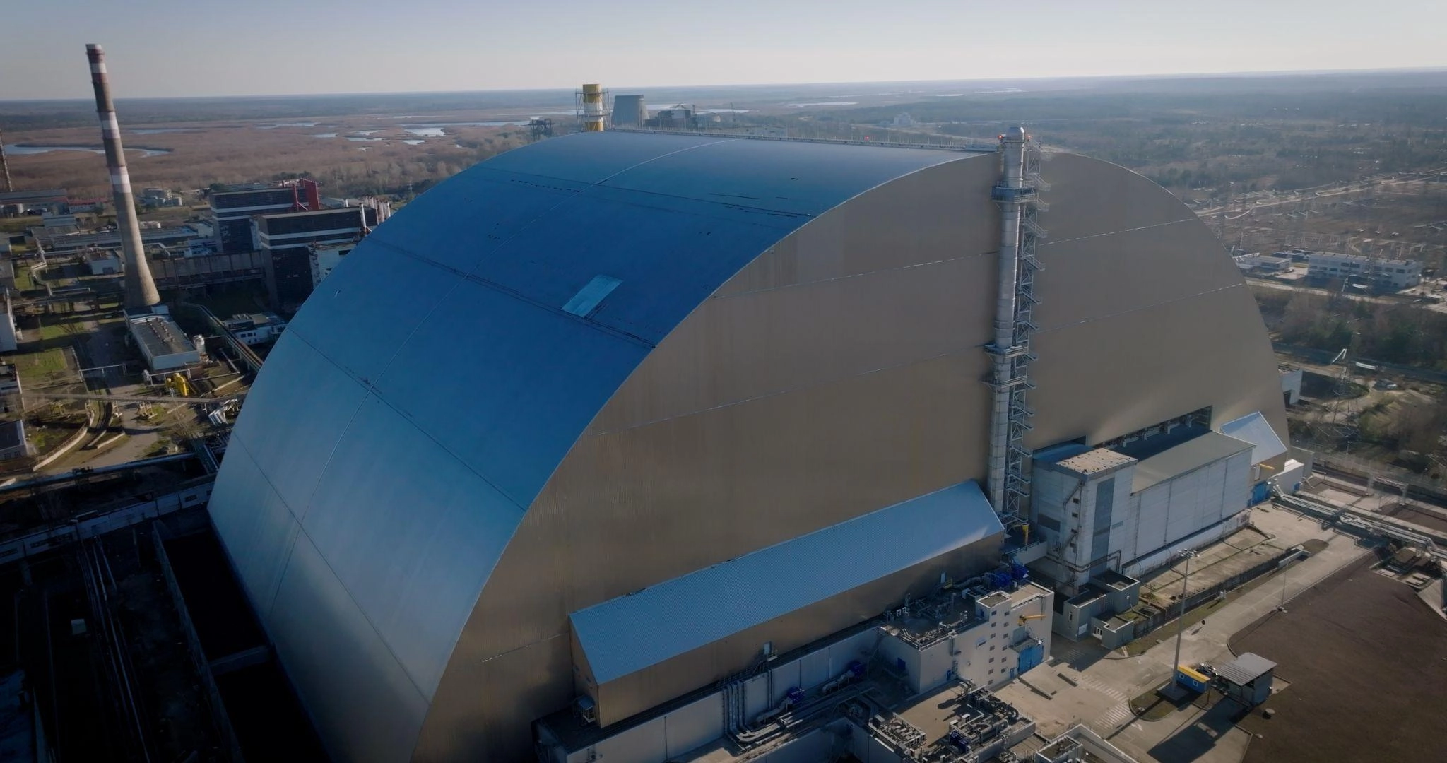 A hole in the cladding of the New Safe Confinement at the Chornobyl Nuclear Power Plant following a Russian drone strike on Feb. 14, 2025, and a temporary cover of the hole after the strike. (Photo courtesy of the EBRD press service)