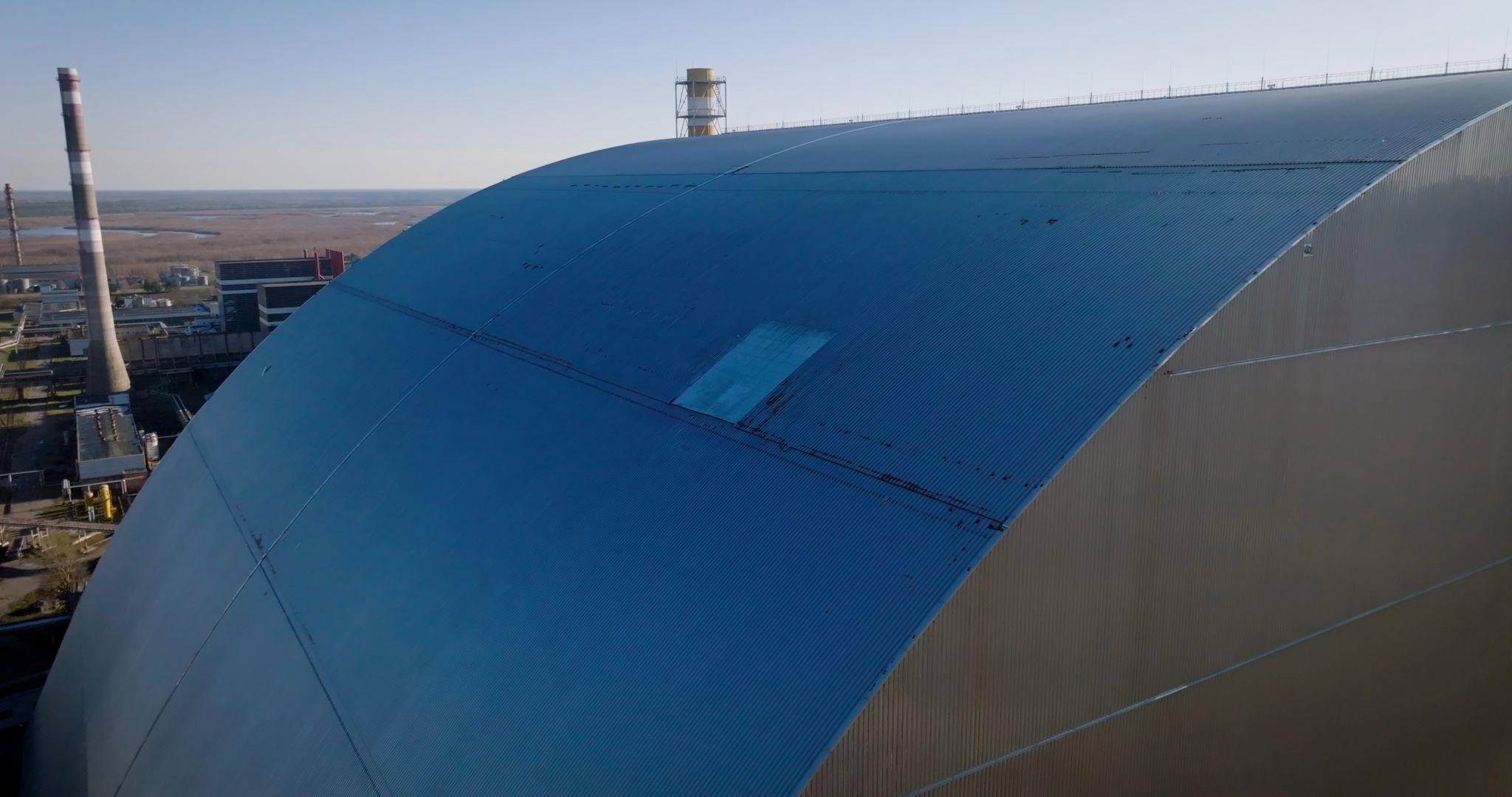 A hole in the cladding of the New Safe Confinement at the Chornobyl Nuclear Power Plant following a Russian drone strike on Feb. 14, 2025, and a temporary cover of the hole after the strike. (Photo courtesy of the EBRD press service)
